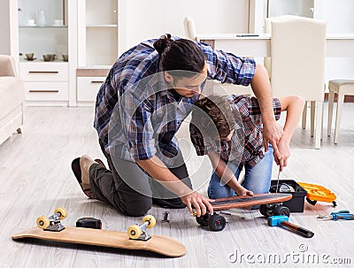 Young father repairing skateboard with his son at home Stock Photo