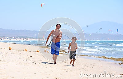 Young father and son running along beach with surfboard Stock Photo