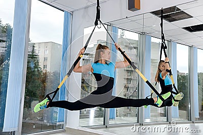 Young female athletic doing exercises training legs with trx straps in fitness gym Stock Photo