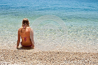 Young female in bikini sitting in shallow sea, left Stock Photo