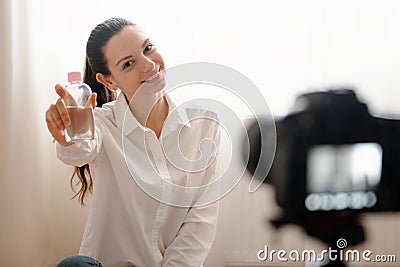 Young female blogger with camera dslr vlogging rewievs body care product in bottle modern online work Stock Photo