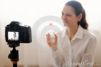 Young female blogger with camera dslr vlogging rewievs body care product in bottle modern online work Stock Photo