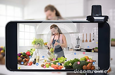 Young female blogger and vlogger and online influencer live streaming a cooking show on social media using a smartphone Stock Photo