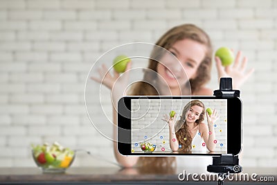 Young female blogger and vlogger and online influencer live streaming a cooking show on social media using a smartphone Stock Photo