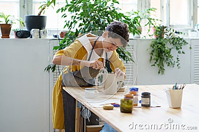 Young female ceramist decorate potter jug after burning. Artisan paining pottery in ceramic workshop Stock Photo