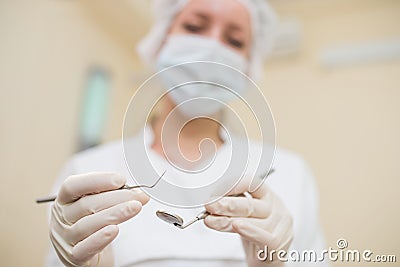 Young female dentist with mirror and periodontal explorer in clinic, closeup, focus on dental instruments Stock Photo