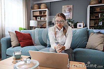 Young female doctor medical worker working from home sitting on sofa having video call with nervous sick patient listening and Stock Photo