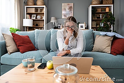 Young female doctor medical worker working from home sitting on sofa having video call with nervous sick patient listening and Stock Photo