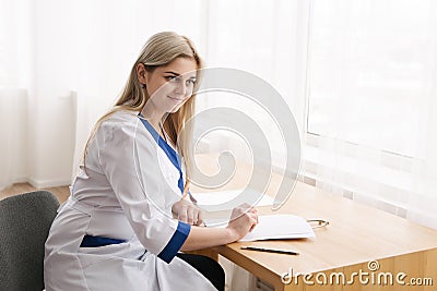 Young female doctor working desk in doctor`s room writing. Stock Photo