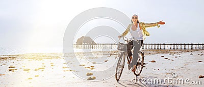 Young female dressed light summer clothes joyfully threw up her hand riding old vintage bicycle with front basket on the low tide Stock Photo