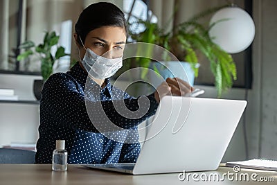 Female employee in face mask disinfect laptop with sanitizer Stock Photo