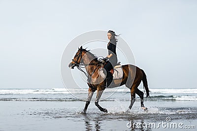 young female equestrian riding horse with ocean Stock Photo