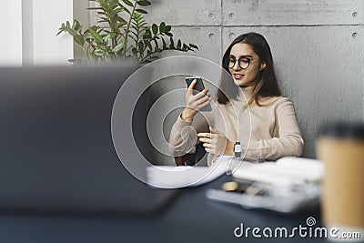 Young female executive sitting at workplace at lunch time and listening to music on smartphone using earphones. Girl using mobile Stock Photo