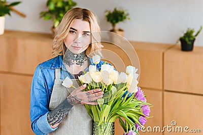 young female florist in apron holding beautiful tulips in vase and looking Stock Photo