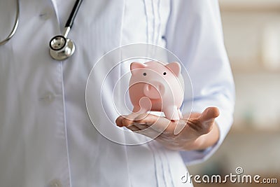 Young female general practitioner holding piggy bank in hands. Stock Photo