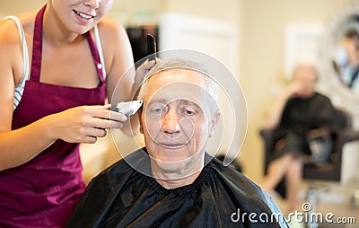 Female hairdresser working hair clipper with older man Stock Photo