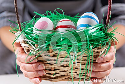 Girl hands with Easter colorful eggs in a wooden basket with green grass Stock Photo