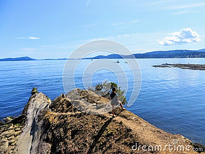 A young female hiker at the end of a path ending at a point overlooking a beautiful blue ocean with islands in the distance Stock Photo