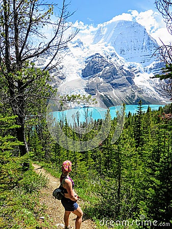 A young female hiker stopped along a hiking trail admiring the beautiful and incredible view of a lake and glacier Stock Photo