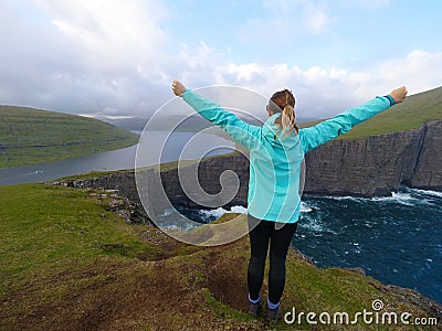 Young female hiker looking at a breathtaking lake from a towering green cliff. Stock Photo