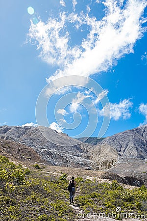 Young female hiker walks through a steep rock mountain and sparse vegetation on a sunny day with blue sky Editorial Stock Photo