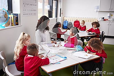 Young female infant school teacher sitting at a table in a classroom with her pupils Stock Photo