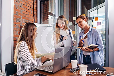 Young female manager sitting at desk pointing at laptop explaining giving tasks to her employees standing writing the Stock Photo