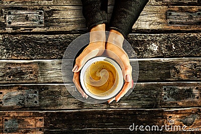 Young female manicured hands holding cup of coffee with fresh foam on old dark rustic wooden table background. Stock Photo