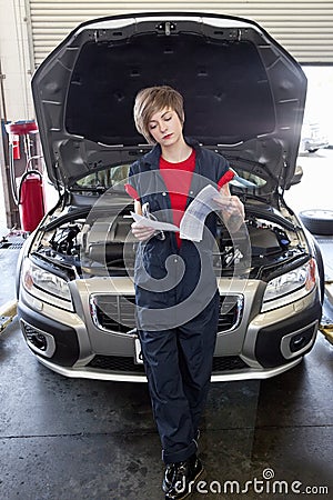 Young female mechanic reading paper with open bonnet of car in garage Stock Photo