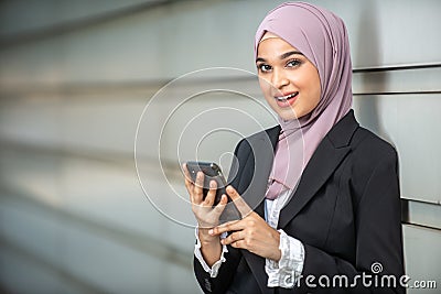 Young Female Muslim Entrepreneur smiling, holding her smartphone. Stock Photo