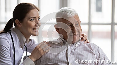 Young nurse hugs old man patient smiling look at distance Stock Photo