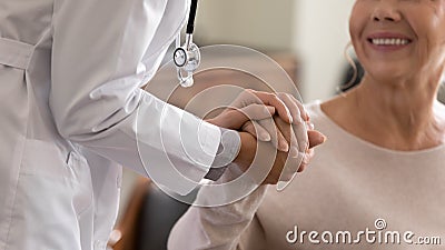 Young female physician holding hand of smiling elderly lady patient Stock Photo