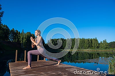 Young female practicing yoga against the sky on a sunrise. Pretty slim woman performs an exercise. Healthcare, meditaion Stock Photo