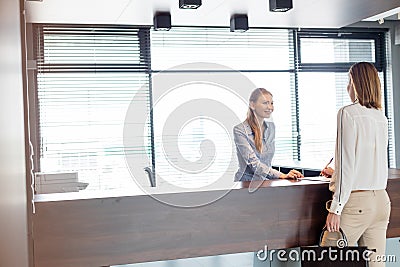 Young female receptionist looking at businesswoman signing document in office Stock Photo