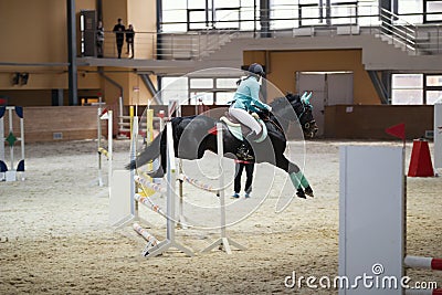 Young female rider on the black stallion jumping over hurdle Editorial Stock Photo