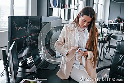 Young female stock brocker is indoors in the office. Many of displays Stock Photo