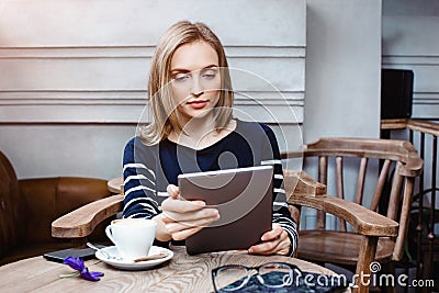 Young female student is chatting on digital tablet with friend while sitting in cafe, attractive woman using laptop Stock Photo