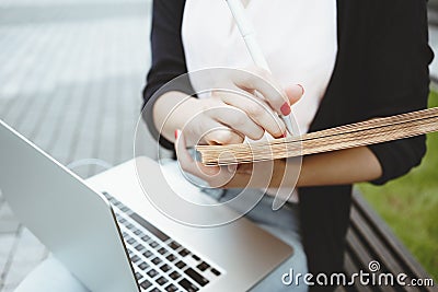 Young female student prepares for a thesis sits on outdoors in urban space opposite university Stock Photo