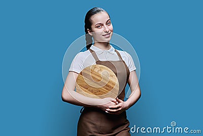 Young female student waitress in an apron with wooden empty tray on blue background Stock Photo