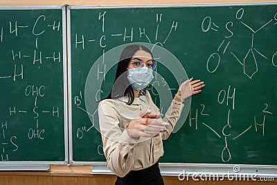 young female teacher in protective mask standing near blackboard Stock Photo