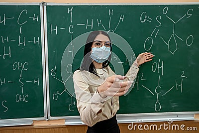 young female teacher in protective mask standing near blackboard Stock Photo