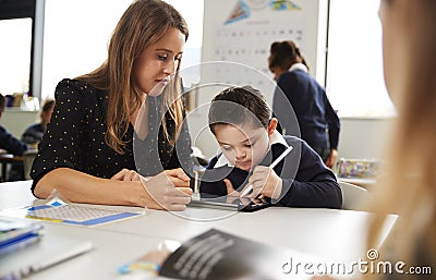 Young female teacher working with a Down syndrome schoolboy sitting at desk using a tablet computer and stylus in a primary school Stock Photo