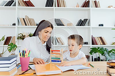 Young female tutor helping little elementary school boy with homework during individual lesson at home Stock Photo