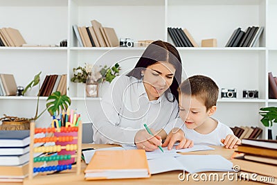 Young female tutor helping little elementary school boy with homework during individual lesson at home Stock Photo