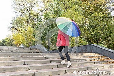 Young female under big colorful umbrella is coming upstairs Stock Photo