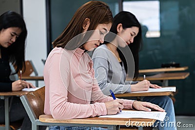 Young female university students concentrate on doing examination in classroom. Girl students seriousely writes the exercise of Stock Photo