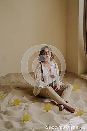 Young female in victorian shirt sitting with rose on the sand and smile Stock Photo