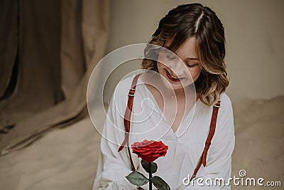 Young female in victorian shirt sitting with rose on the sand and smile Stock Photo