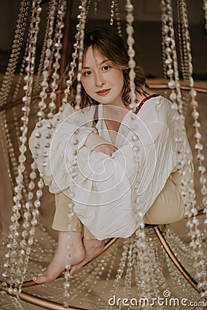 Young female in victorian shirt sitting in giant crystal chandelier and smile Stock Photo