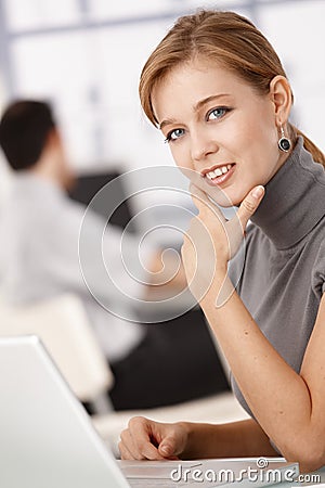 Young female working on laptop in office smiling Stock Photo